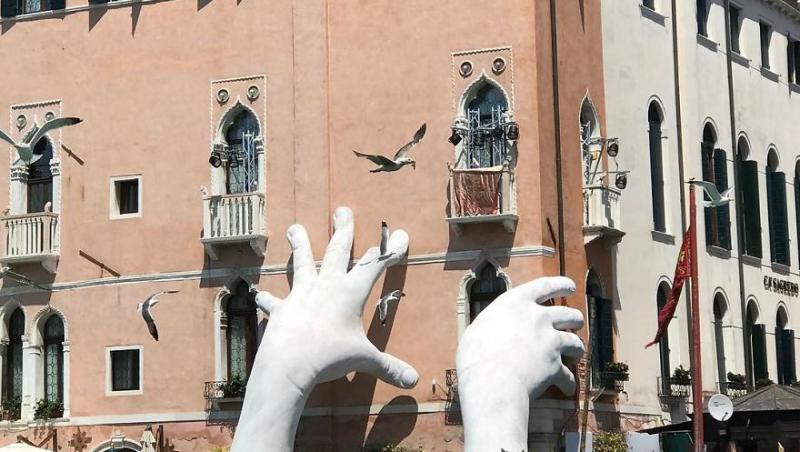 Degradarea și schimbările climatice pot ”închide” cel mai vizitat oraș din Europa! Două mâini uriaşe de copil sprijină o clădire din Veneția