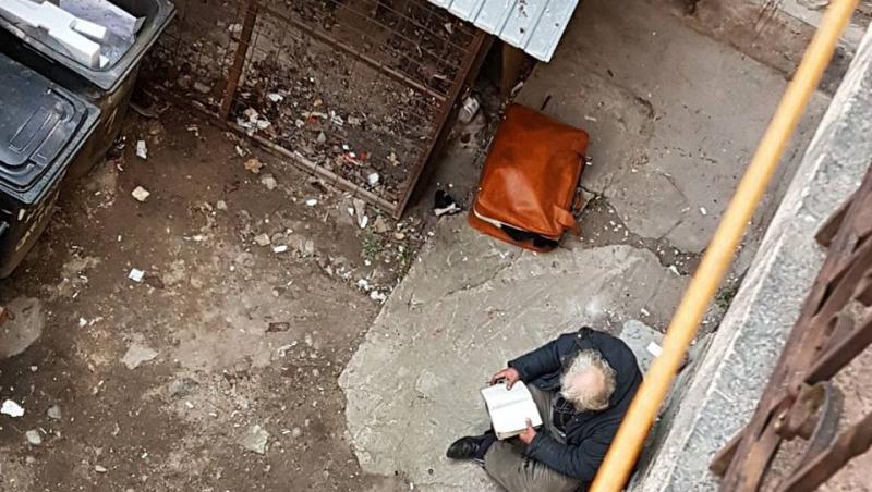 O carte și o valiză, întreaga avere a unui bătrân! Abandonat lângă ghena unui bloc, citește, în singurătate: 
