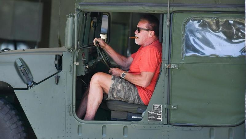 Arnold Schwarzenegger, fotografiat de paparazzi la bordul unui Hummer. Actrorul are trabuc în gură și este îmbrăcat într-un tricou roșu și pantaloni scurți