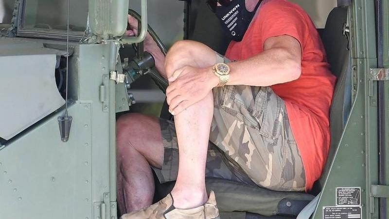 Arnold Schwarzenegger, fotografiat de paparazzi la bordul unui Hummer. Actrorul poartă mască de protecție și este îmbrăcat într-un tricou roșu și pantaloni scur