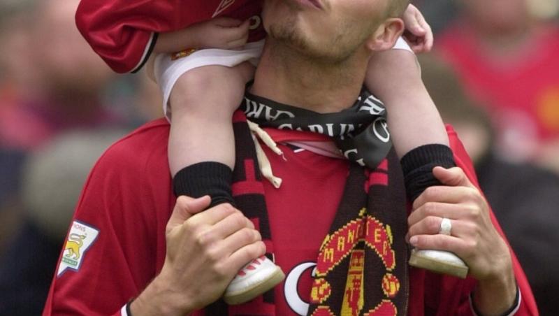 David Beckham, pe terenul de fotbal, cu fiul sau pe umeri, uniforma rosie
