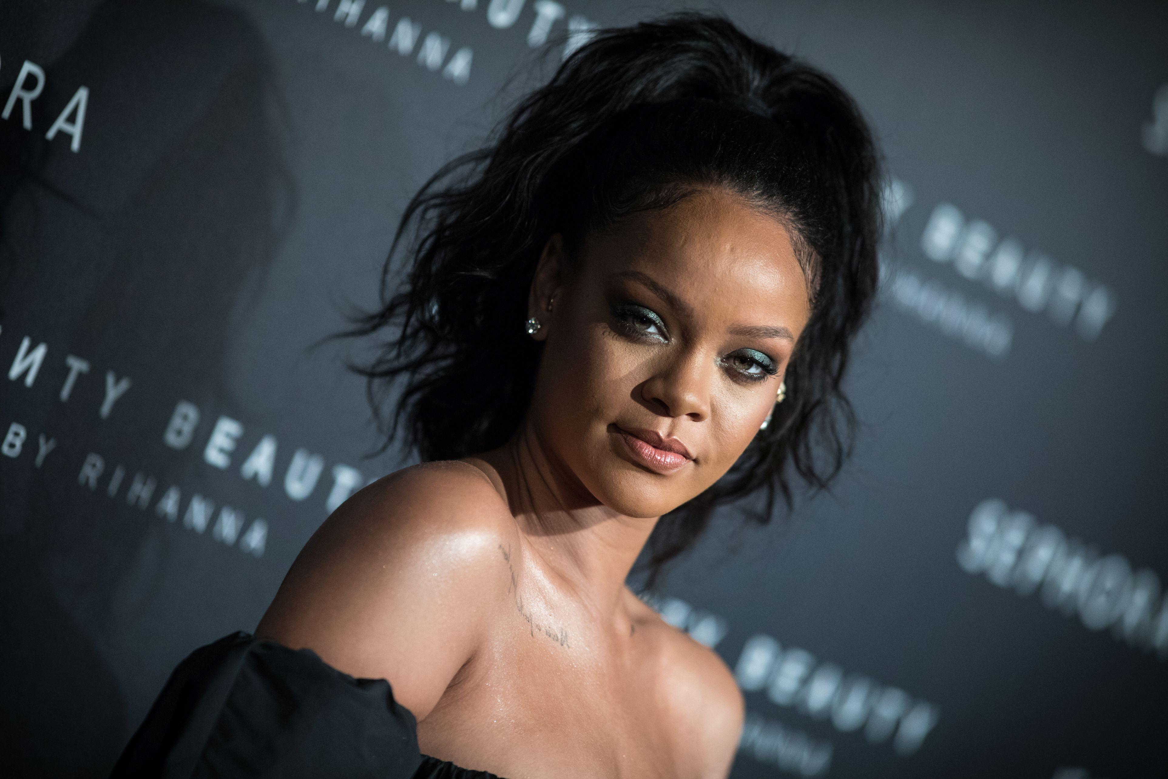 Rihanna, îmbrăcată într-o rochie neagră, cu ochii puternic conturați și părul prins într-o coadă în vârful capului