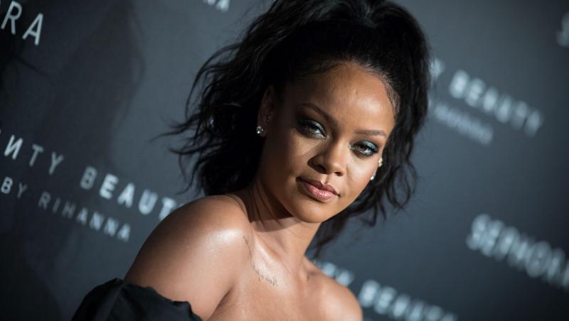 Rihanna, îmbrăcată într-o rochie neagră, cu ochii puternic conturați și părul prins într-o coadă în vârful capului