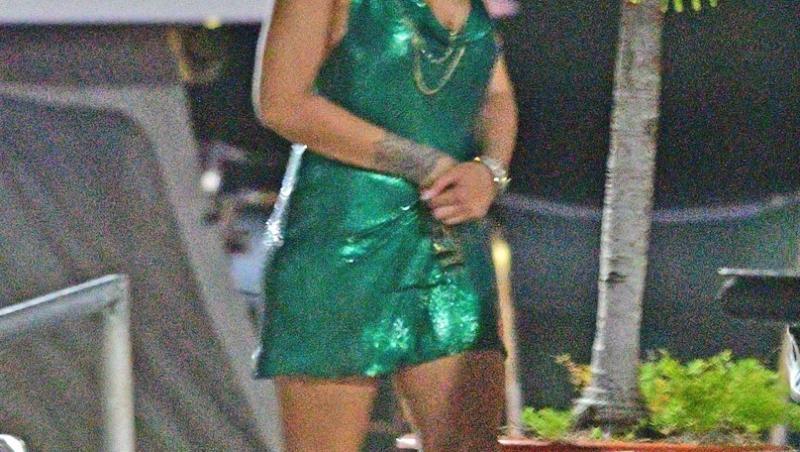 Rihanna, într-o rochie verde, accesorizată cu bijuterii masive și șapcă pe cap, poartă mască de protecție