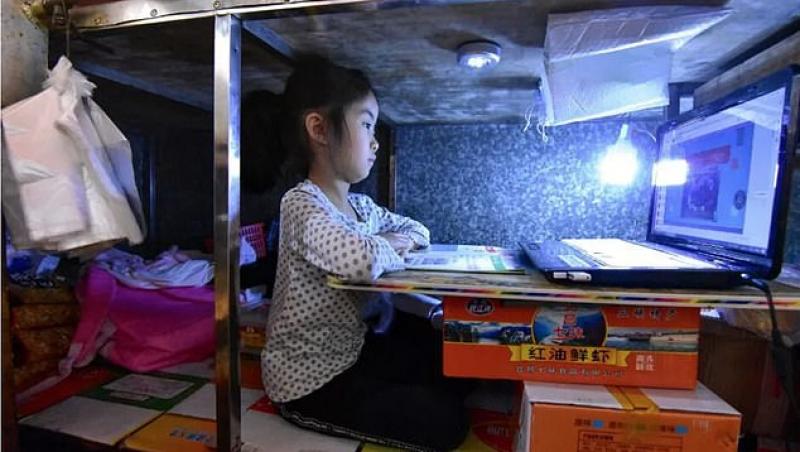 O fetiță își face temele sub taraba la care mama ei vinde pește