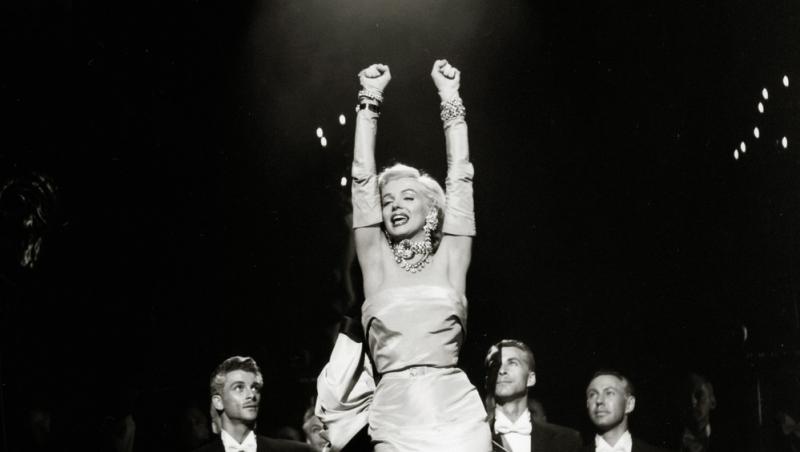 Marilyn Monroe într-o rochie lungă, cu brațele în aer