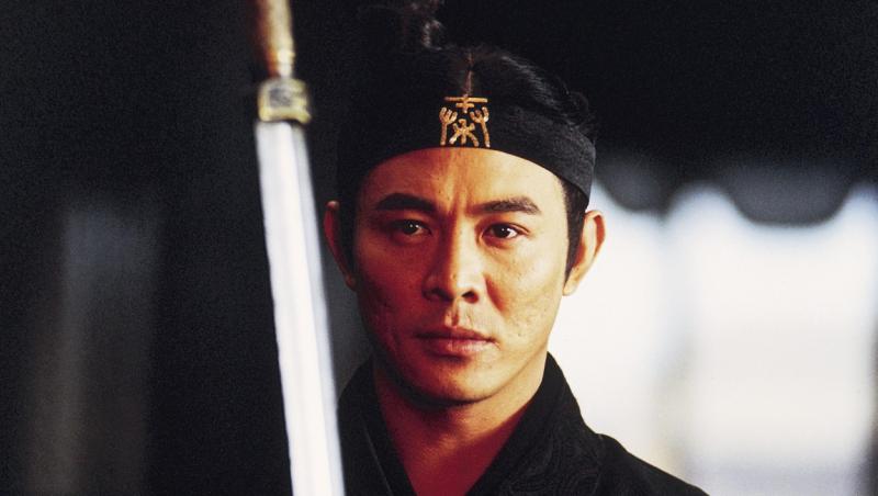 Jet Li, într-o scenă din filmul ''Hero'' (2002), privește atent către o sabie, având pe cap o banderolă și părul prins în coc