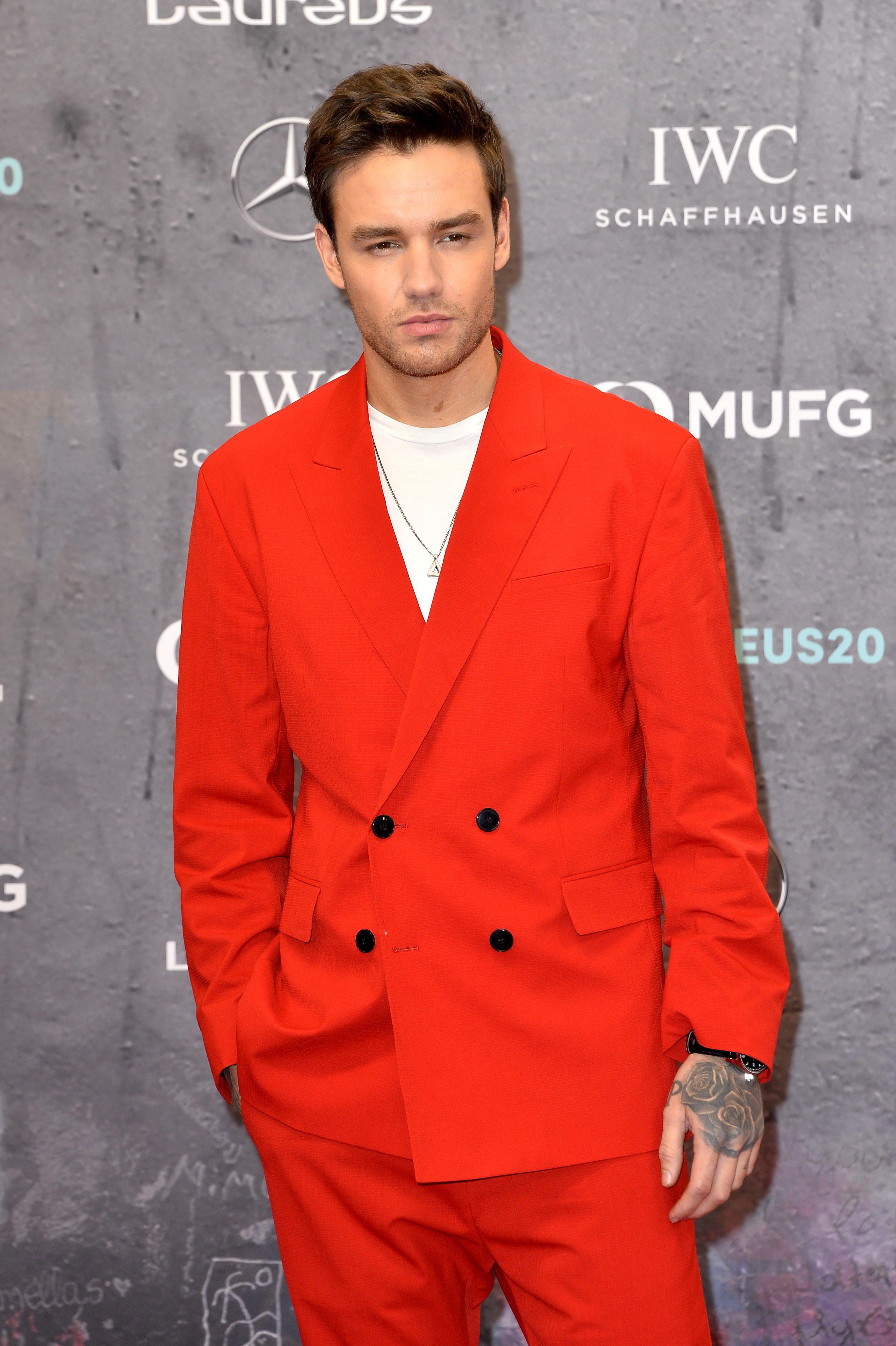 Liam Payne, privește direct în obiectivul aparatului de fotografiat și este îmbrăcat cu un sacou roșu, cu două rânduri de nasturi
