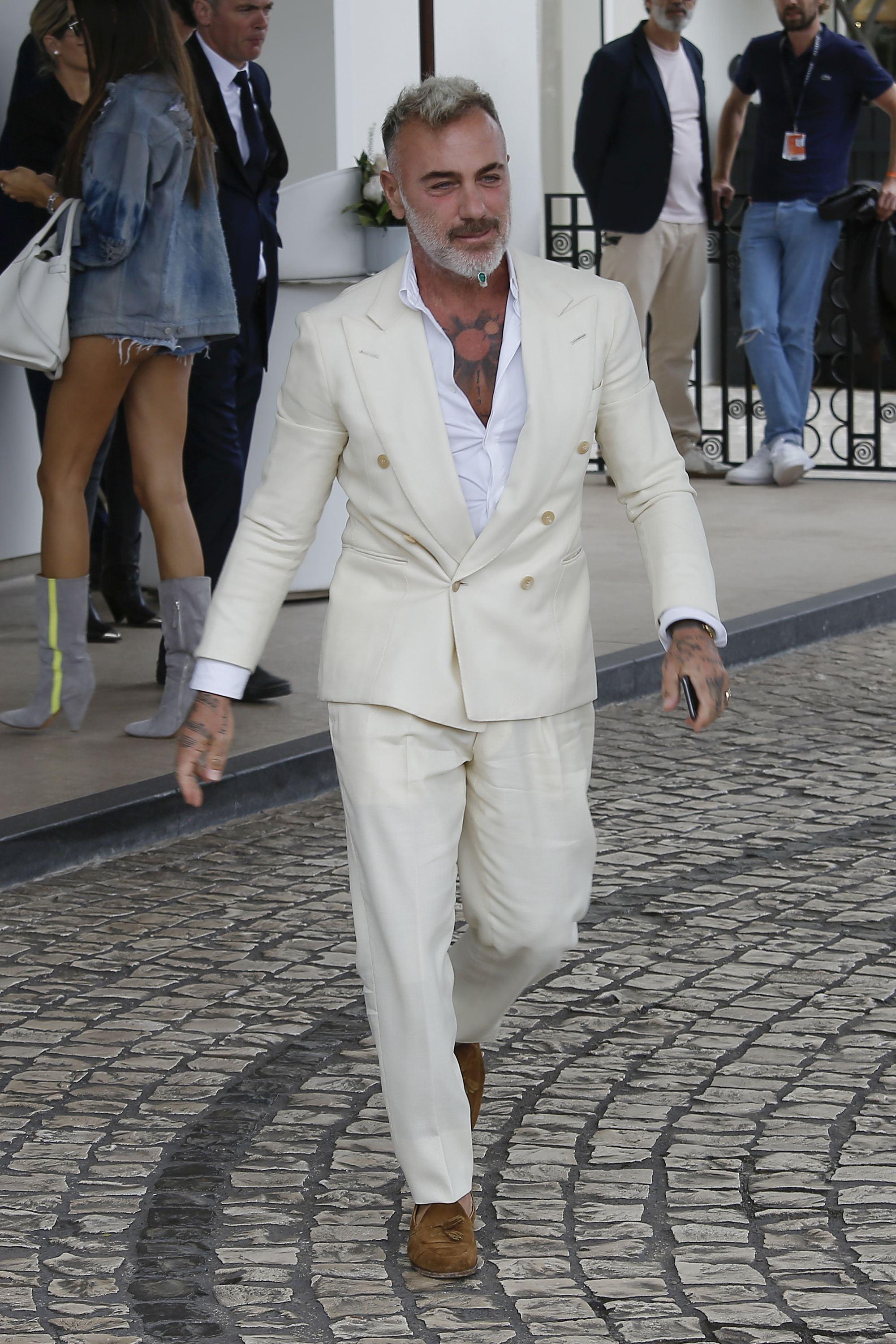 Gianluca vacchi, imbracat intr-un costum alb, fotografiat cand merge