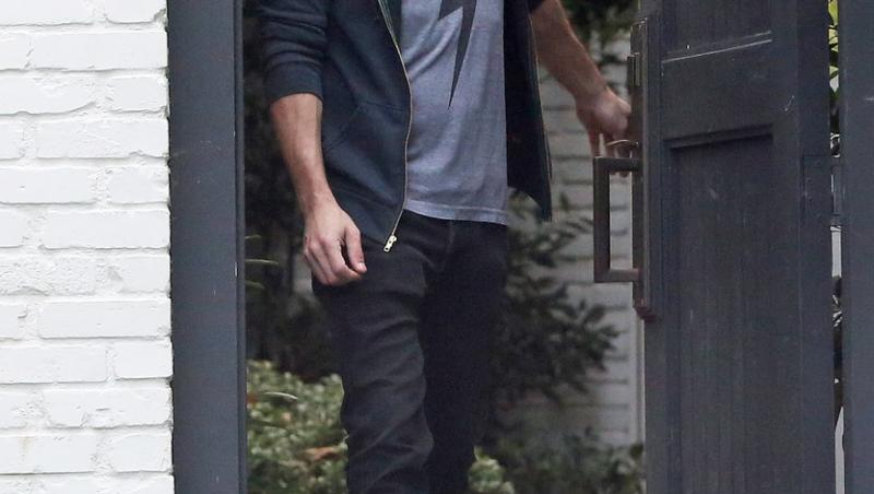 Ben Affleck cu parul lungi si barba deasa, imbracat intr-un tricou albastru si blugi negri, iese pe poarta