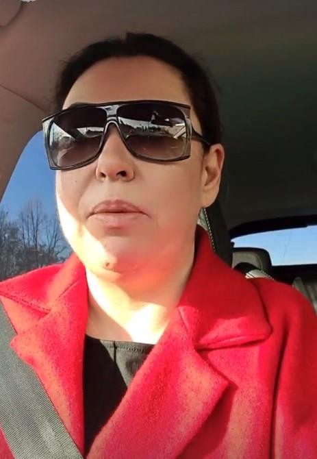 Oana Roman, cu un palton roșu, ochelari de soare și părul prins, în mașină