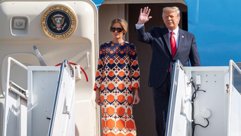 Donald Trump, purtând costum și cravată și Melania Trump într-o rochie cu negru și portocaliu, coborând din avion, în Flordia