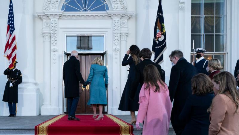 Joe Biden, îmbrăcat la costum și Jill Biden, cu un palton albastru, în fața unor uși închise, la Casa Albă