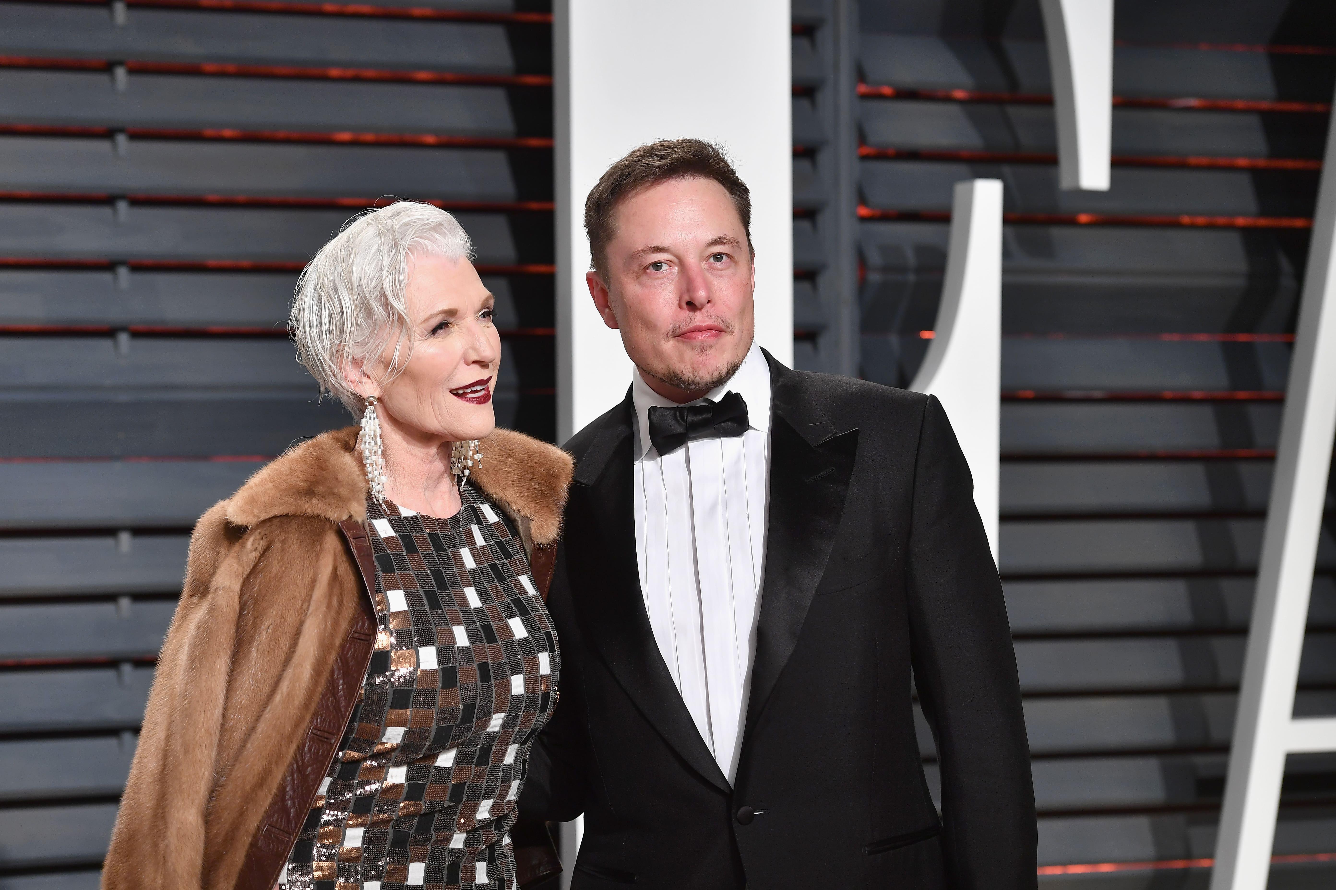 Elon Musk si mama lui pe covorul rosu, el costum negru camasa alba, ea rochie gri cu haina maro