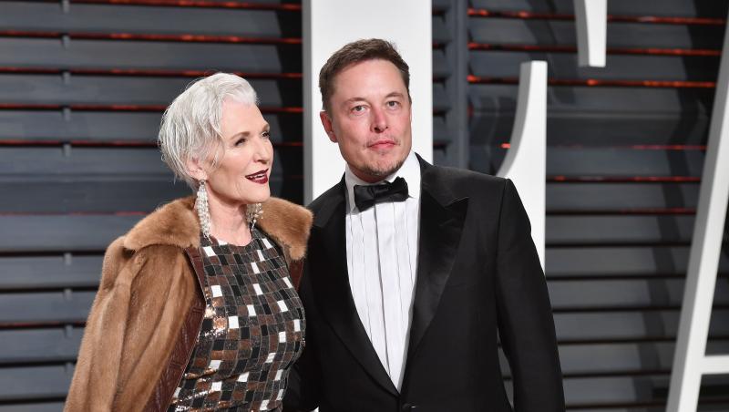 Elon Musk si mama lui pe covorul rosu, el costum negru camasa alba, ea rochie gri cu haina maro