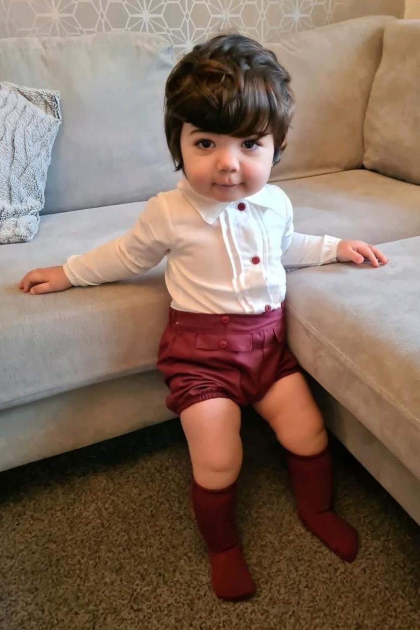 Reign Butler, la vârsta de un an și trei luni, îmbrăcat în pantaloni scurți roșii și bluză albă