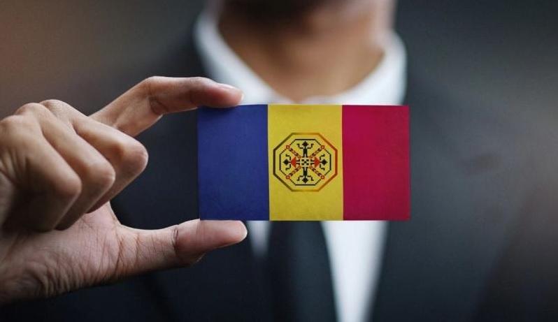 Poză ilustrativă cu mâna unui bărbat ținând între degete un steag al României în miniatură