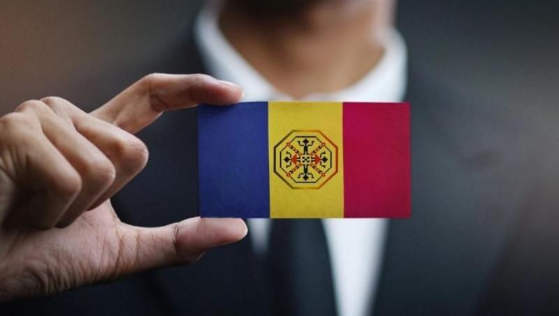 Poză ilustrativă cu mâna unui bărbat ținând între degete un steag al României în miniatură