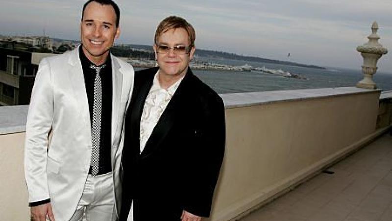 Elton și soțul lui, David Furnish, imbracati la costum. Elton Jon, in negru, sotul, in alb