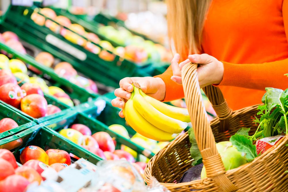 femeie cu bluza portacalie care luat banane de pe raft din supermarket