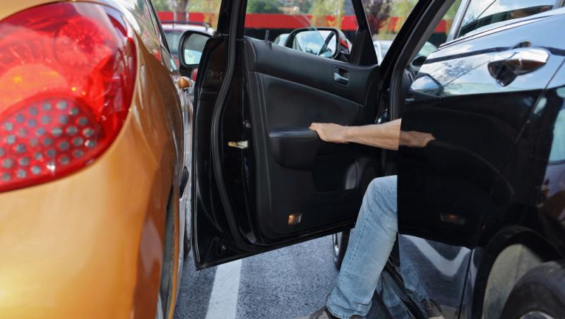 barbat care deschide portiera unei masini negre langa una portocalie