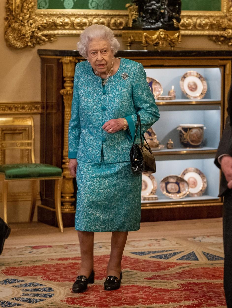 regina elisabeta imbracata intr-un costum, cu geanta pe mana si pantofi negri