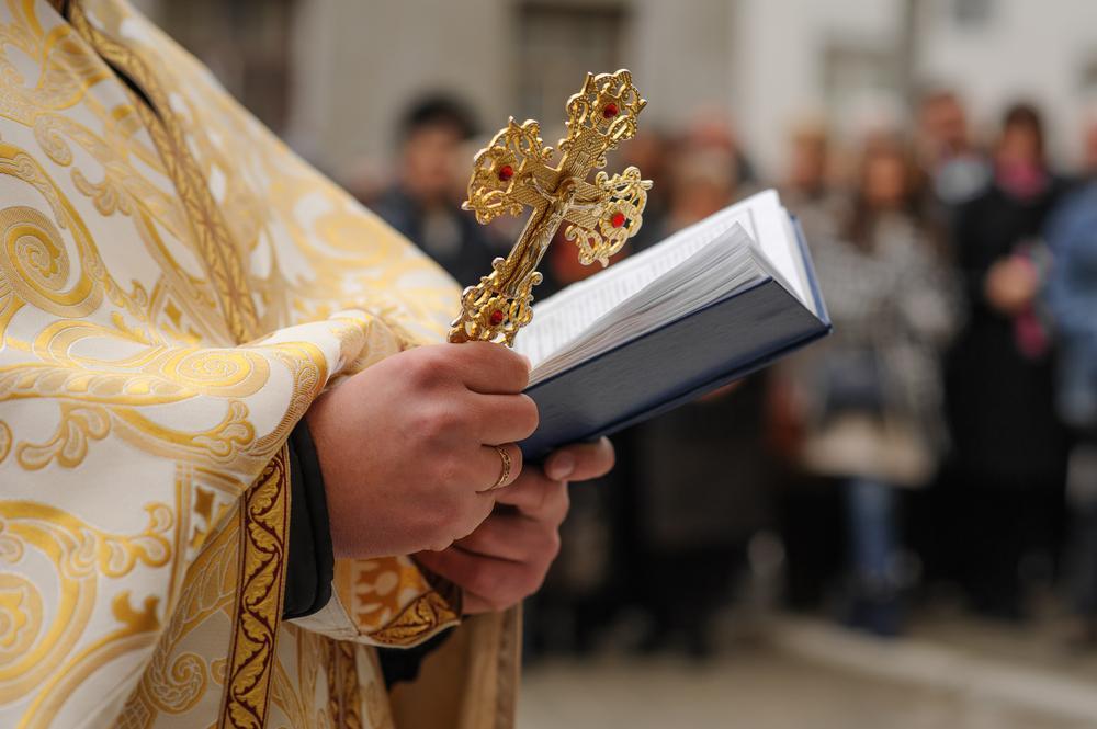 preot care ține in maini o carte sfanta, din care rosteste rugaciuni și cruce