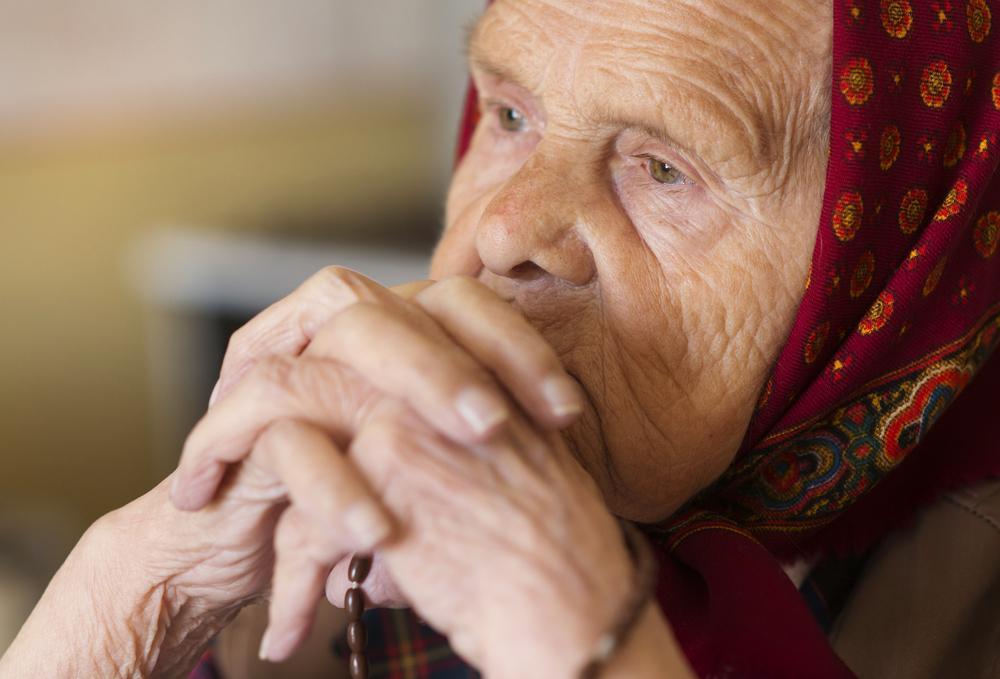 o bunică care sta cu mainile impreunate, ce priveste concentrata în timpul unei rugaciuni și ii pomeneste pe cei morti