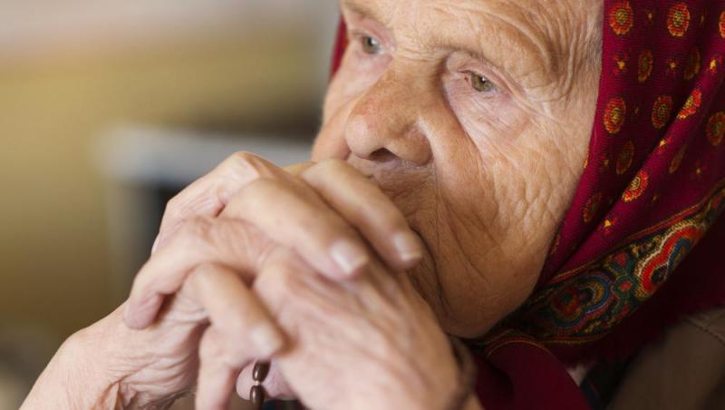 o bunică care sta cu mainile impreunate, ce priveste concentrata în timpul unei rugaciuni și ii pomeneste pe cei morti