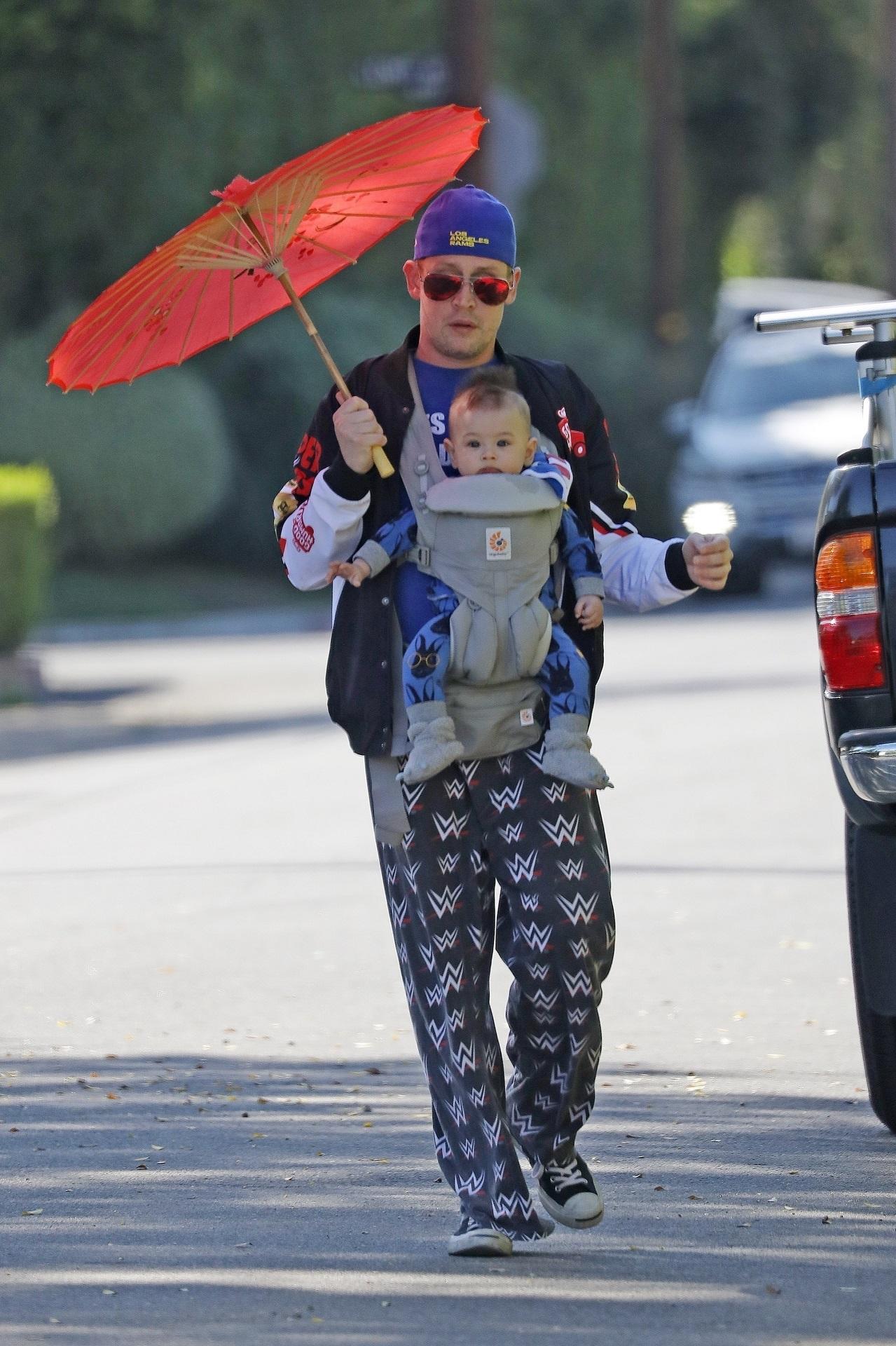 macaulay culkin, pe stradă, cu fiul lui, dakota. are o umbrelă asiatică portocalie și merge pe stradă