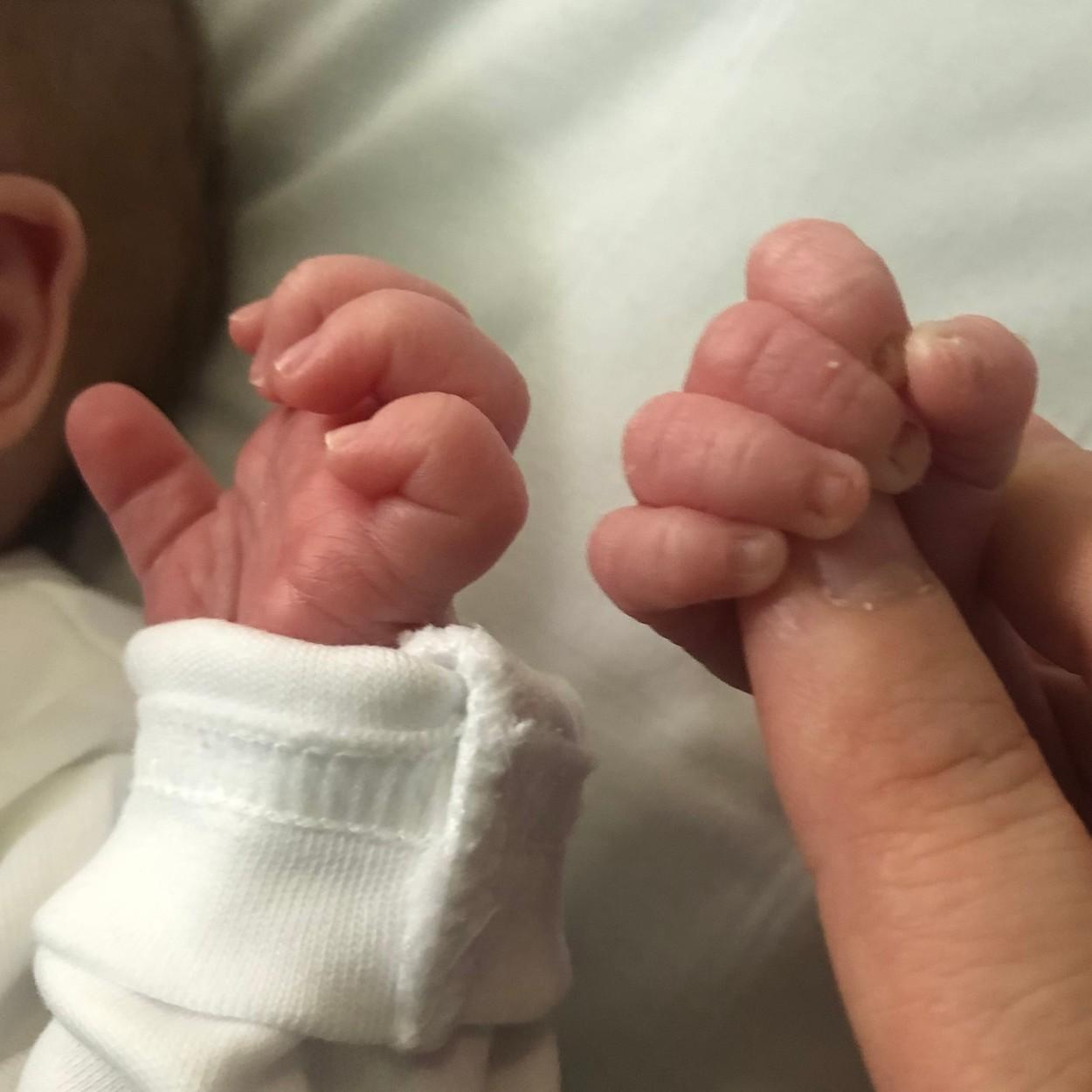doua maini de bebelus iar in una dintre ele se afla un deget de adult