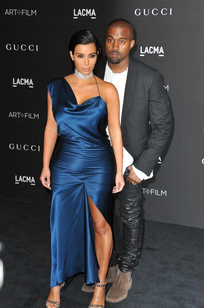 Kanye West imbracat intr-un sacou gri cu camasa alba alaturi de kim kardashian care poarta o roche eleganta albastra