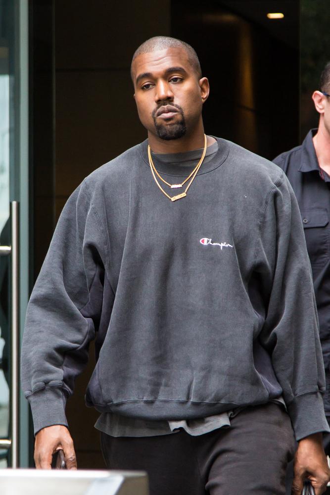 Kanye West intr-o bluza gri cu un lant de aur la gat merge pe strada si este fotografiat