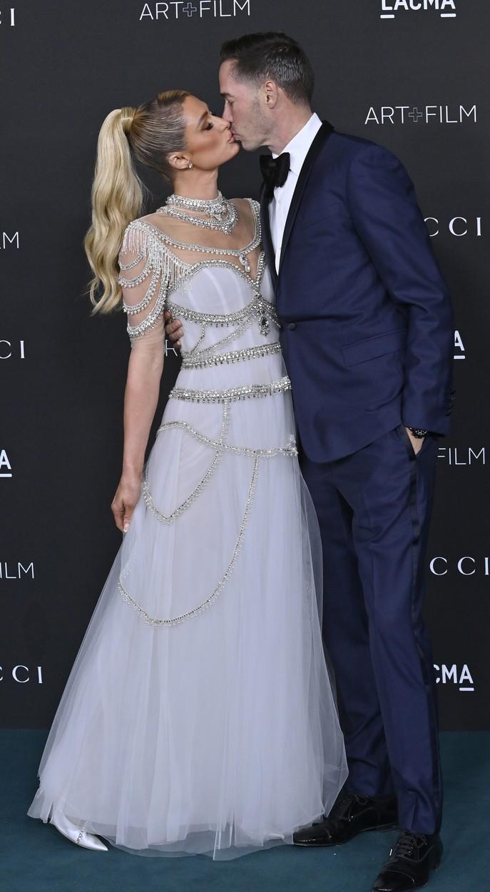 Paris Hilton imbracata intr-o rochie lunga eleganta il saruta pe carter reum care poarta un costum albastru