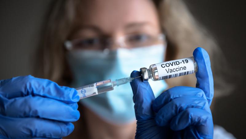 femeie care tine cu mainile o seringa si o doza de vaccin anti covid-19