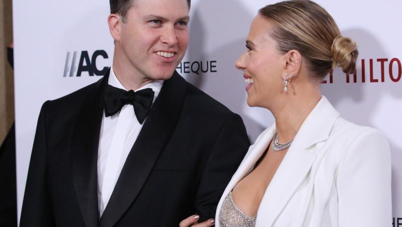 Scarlett Johansson si sotul ei se privesc si isi zambesc indragostiti, pe covorul rosu, unde ea este imbracat intr-un costum alb si el poarta un costum negru.