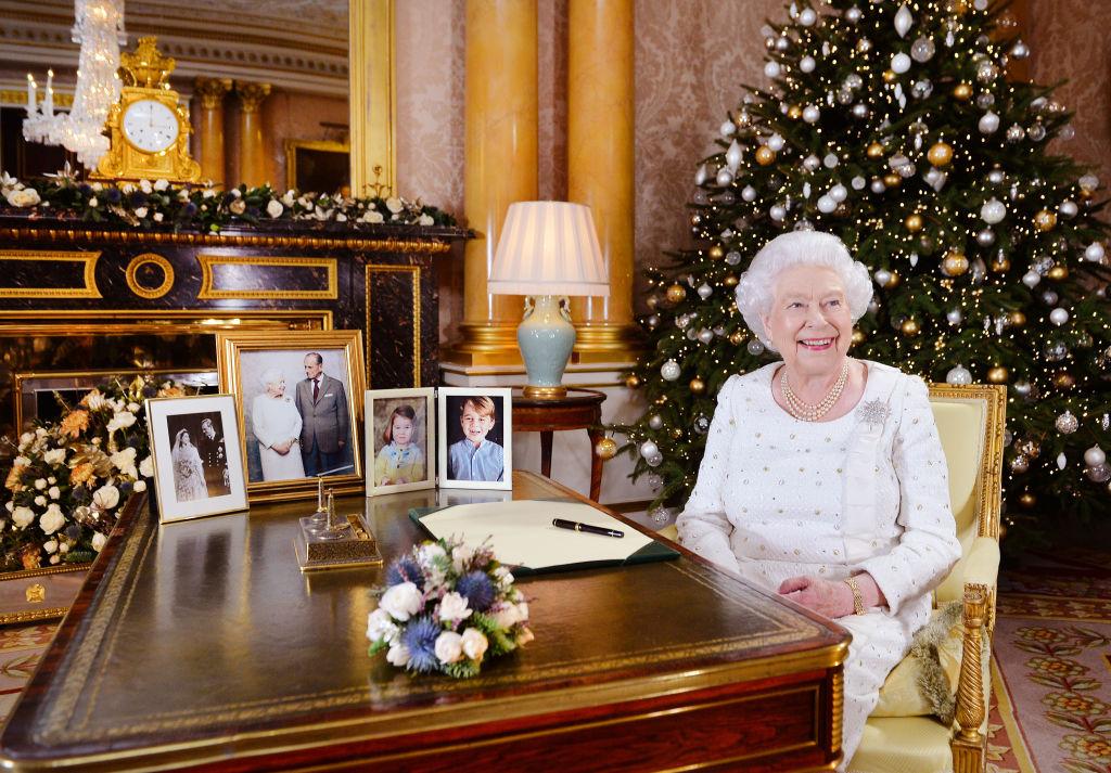 regina elisabeta a II-a a marii britanii imbracata intr-o rochie alba sta la birou intr-un cadru decorat de craciun