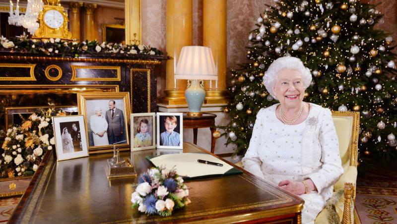regina elisabeta a II-a a marii britanii imbracata intr-o rochie alba sta la birou intr-un cadru decorat de craciun