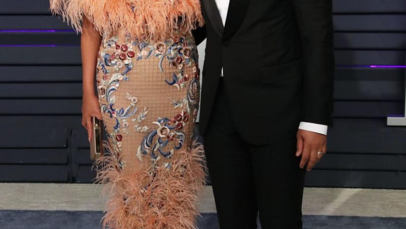 Chrissy Teigen imbracata in rochie lunga, in culori deschise, alaturi de sotul ei, John Legend, la un eveniment oficial, ambii imbracati elegant