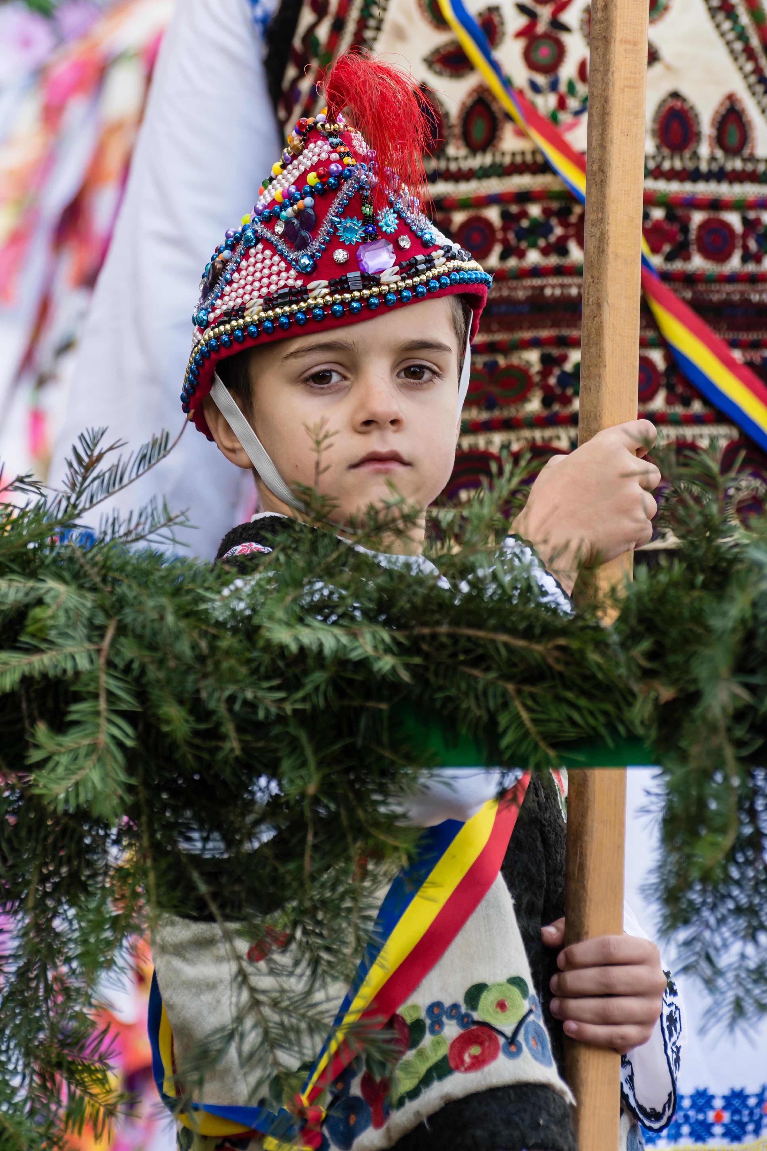 baietel imbracat in costum traditional care tine un obiect din lemn in mana