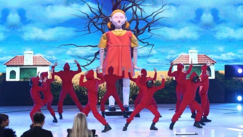 dansatori imbracati in uniforme rosii din Squid game danseaza in fata papusii din serial, pe scena de la Revelionul starurilor