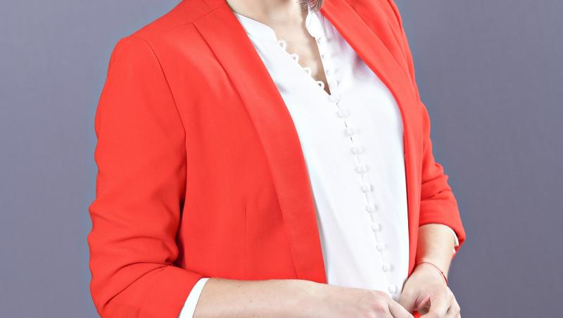 Mirela Vaida, poză de studio, poartă bluză și pantaloni albi și un sacou roșu coral