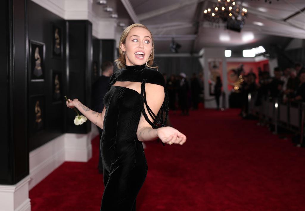 Miley Cyrus, cu părul lung, într-o rochie neagră, mulată, de catifea, la un eveniment