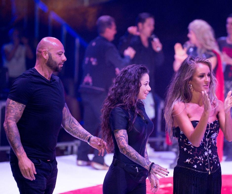 Giani Kiriță intr-un tricou negru pe scena circului Bellucci și tine o ruleta in mana, alaturi de Roxana Vancea si Diana Munteanu