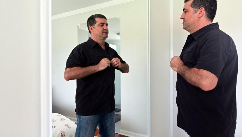 Imagine ilustrativă cu un bărbat îmbrăcându-se în fața unei oglinzi