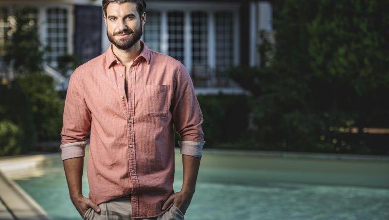 Andi Constantin de la „Burlacul”, îmbrăcat cu o cămașă roz și pantaloni, stând lângă o piscină