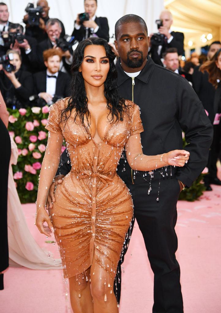 Kim Kardashian imbracata intr-o rochie portocalie, alături de Kanye West, care are o tinuta neagra