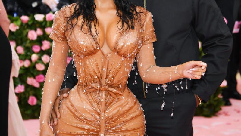 Kim Kardashian imbracata intr-o rochie portocalie, alături de Kanye West, care are o tinuta neagra