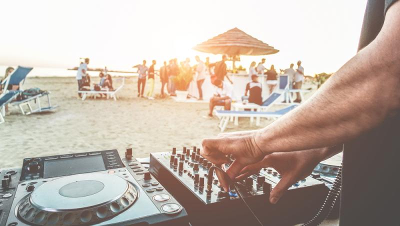 Un DJ, care pune muzică, iar pe plaja oameni care petrec