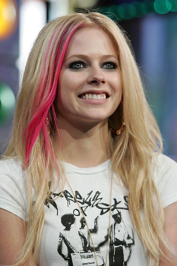 Avril Lavigne într-un tricou alb, are părul blond și o șuviță roz